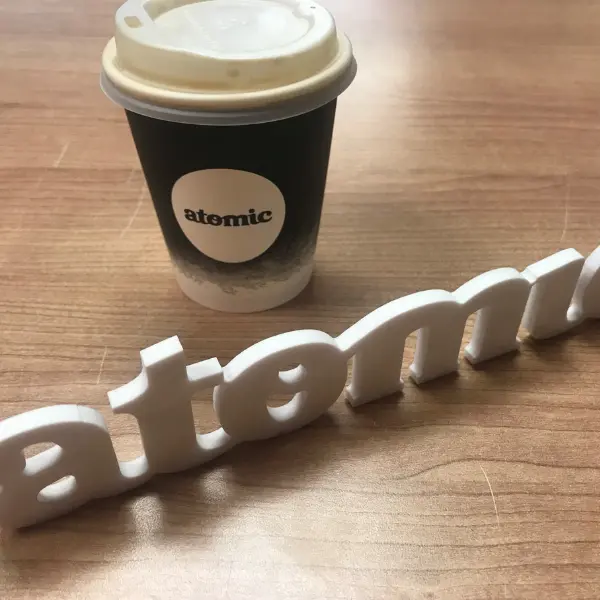 Black and white coffee cup labeled “atomic” placed on a wooden surface, with a matching 3D-printed “atomic” logo in front, showcasing cohesive brand design.